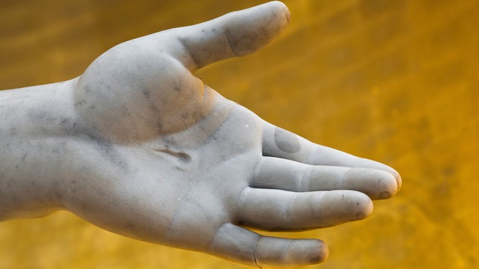 Et nærbillede af en forvitret hånd, der rækker ud over et felt af gyldne aks.