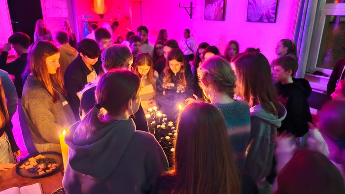 Eine lebhafte Gruppe versammelt sich drinnen bei Kerzenlicht, teilt Essen und Gespräche unter violettem Licht.