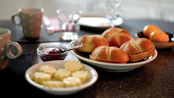 Ein gemütliches Frühstücksarrangement mit Gebäck, Butter, Marmelade und Kaffee auf einem Holztisch.