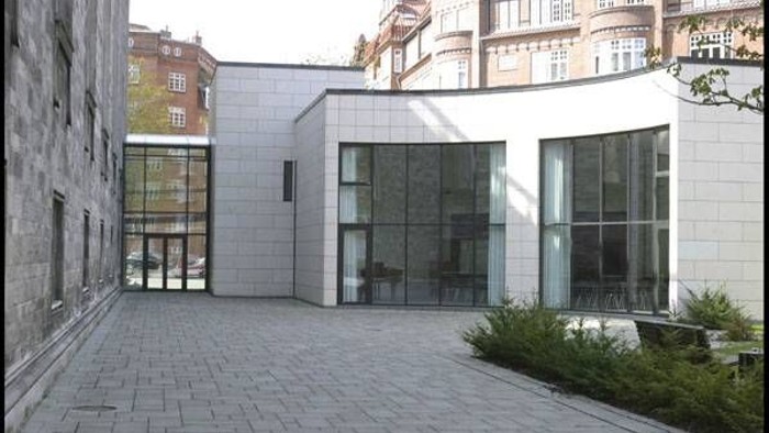 Et moderne bygning med store glassvinduer og grønne planter ved indgangen.