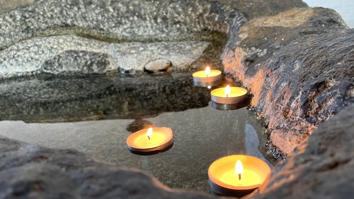 Fire tændte stearinlys placeret på en tekstureret stenoverflade med vandrefleksioner.