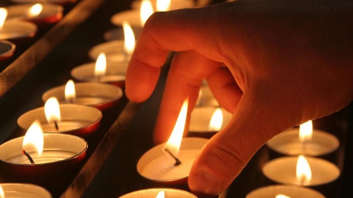 Eine Hand, die eine Kerze unter vielen brennenden Kerzen anzündet.