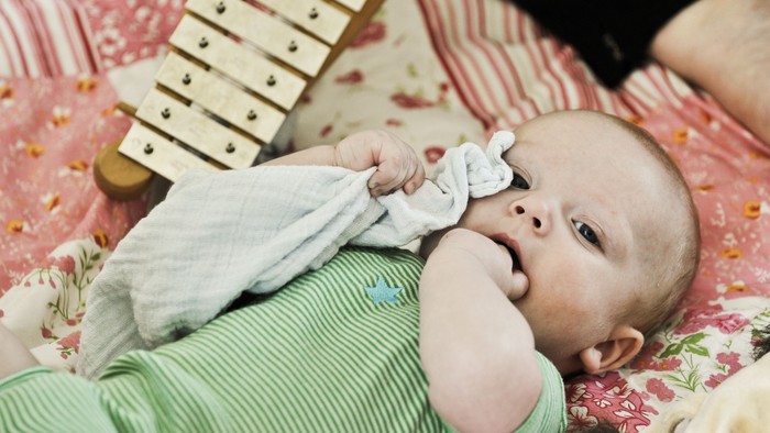 Et spæd barn ligger på en blomsteret sengbede og suger på en sværde.