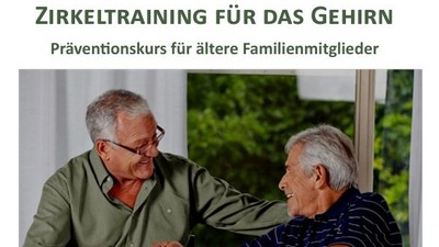 Zwei ältere Männer sitzen an einem Tisch und lachen, während sie etwas auf einem Stück Papier betrachten.