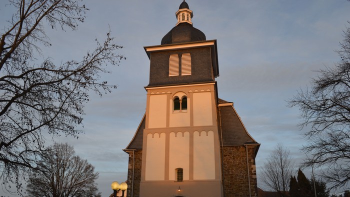 Ein hell erleuchteter Kirchturm vor einem bewölkten Himmel
