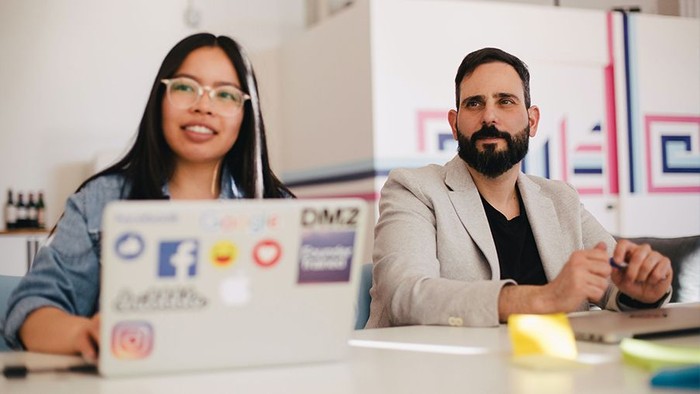Frau mit Laptop und Mann sitzen an dich und schauen auf.