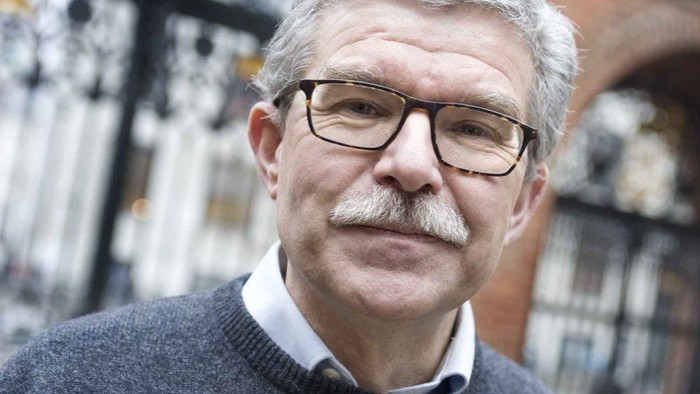 En ældre mand med briller og mæltebær ser direkte i kameraet.