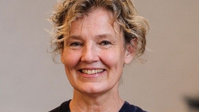 En smilende kvinde i et mørkt, mønstret kimono-lignende tøjstykke med kort, krøllet hår.