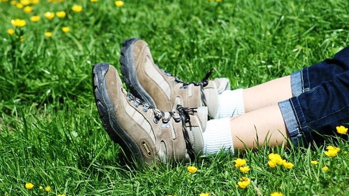 Abgenutzte Wanderschuhe, die auf üppigem grünem Gras mit gelben Blumen ruhen.