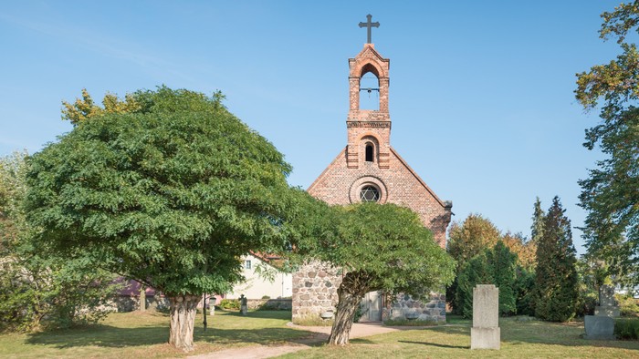 Kirchengelände mit Kreuz und Bäumen unter blauem Himmel