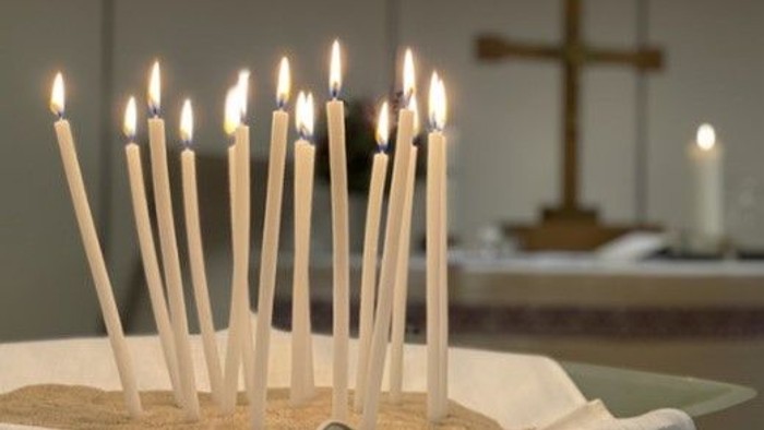 Stearinlys tændt i sandet, kors i baggrunden