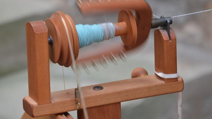 Handgefertigtes Spinnrad mit buntem Garn, das auf eine Spindel aufgewickelt wird.