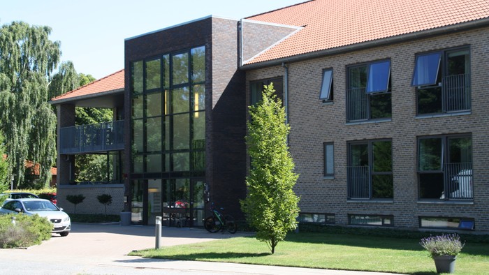 Moderne kontorbygning med store vinduer og grønne omgivelser