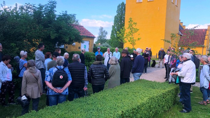 En gruppe af mennesker står i en trækirkegård foran en gul kirke.