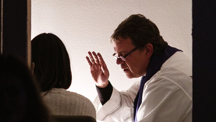 Ein Mann in weißem Anzug winkt auf einer Bühne.