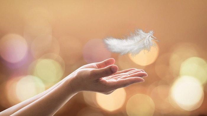En hånd, der forsigtigt holder en hvid fjer mod en blød, lysende baggrund.