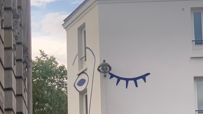 En blå og hvid tegnelse af et øje og en snak på siden af et hvidt bygning.