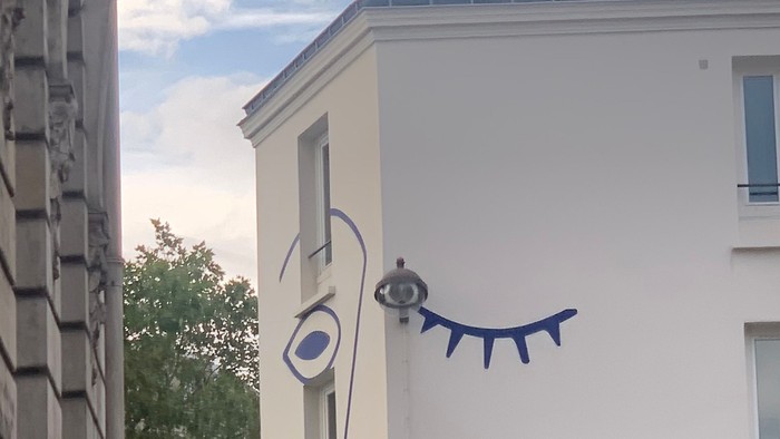 En blå og hvid tegnelse af et øje og en snak på siden af et hvidt bygning.