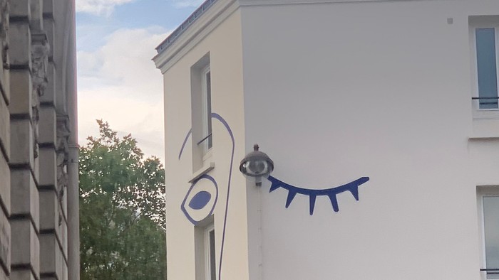 En blå og hvid tegnelse af et øje og en snak på siden af et hvidt bygning.