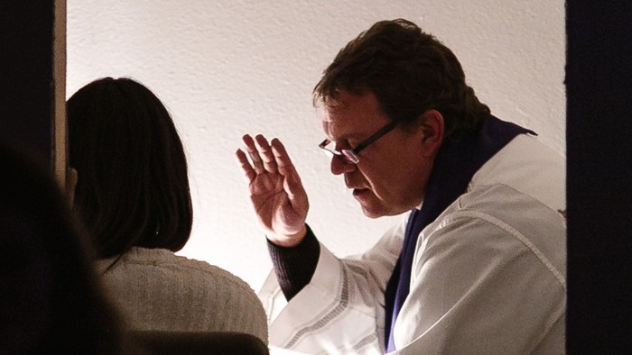 Ein Mann in weißem Anzug winkt auf einer Bühne.