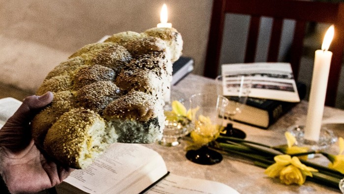 En person holder en stor kage med nødder mens der er lysede lygter og blomster på bordet.