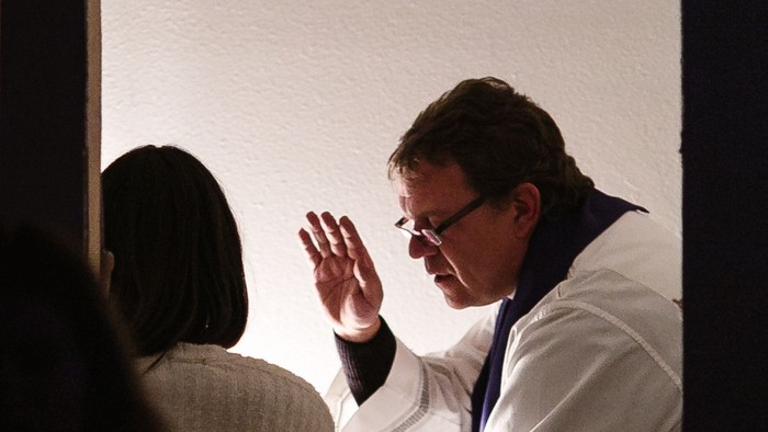 Ein Mann in weißem Anzug winkt auf einer Bühne.