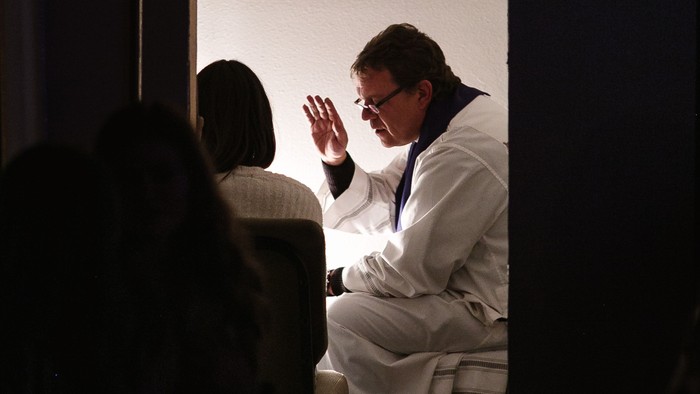 Ein Mann in weißem Anzug winkt auf einer Bühne.