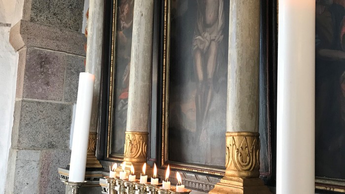 En altertavle med lysstake og blomster i kirke