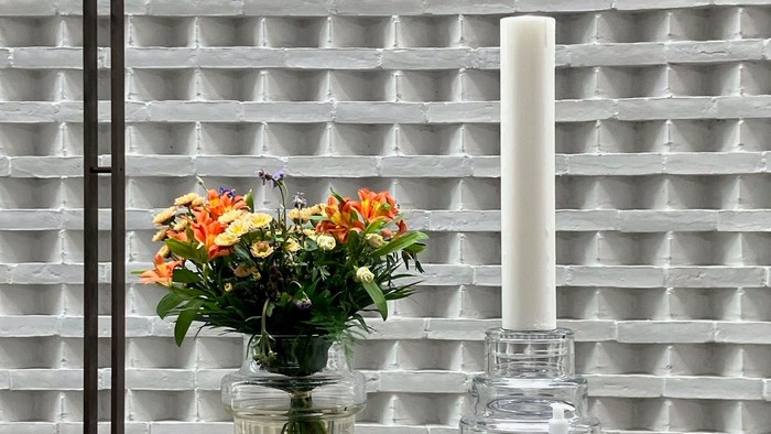 Blomster og lysestage på bord foran muret væg