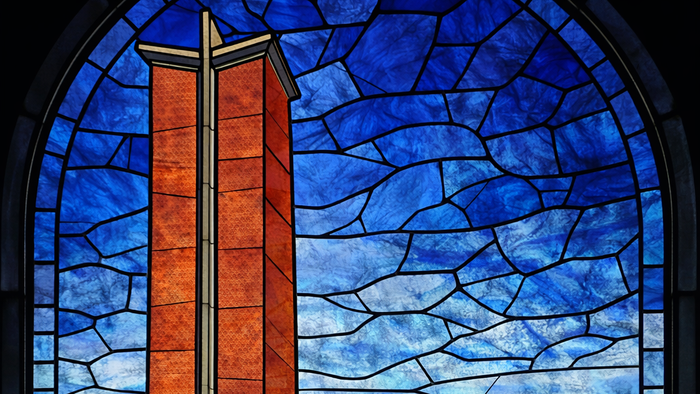 Farvet glasvindue, der forestiller et kirkespir omgivet af blomstrende vilde blomster under en blå himmel.