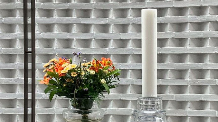 Blomster og lysestage på bord foran muret væg