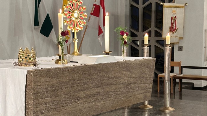 Eleganter Kirchenaltar, geschmückt mit Kerzen, Fahnen, Blumengestecken und religiösen Verzierungen auf einem Marmorboden.