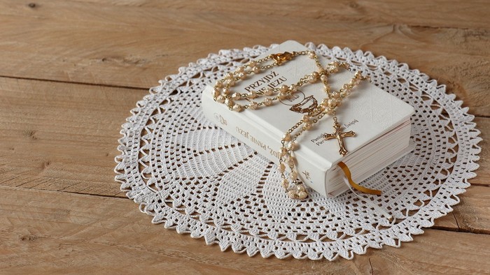 En hvid doilie med en halskæde og en liten bog der ligger på en træflade