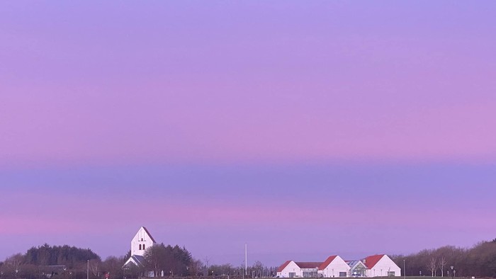 En rødlysende solgang over en åben landskab med en kirke og en gruppe svane.