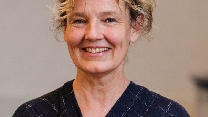 En smilende kvinde i et mørkt, mønstret kimono-lignende tøjstykke med kort, krøllet hår.