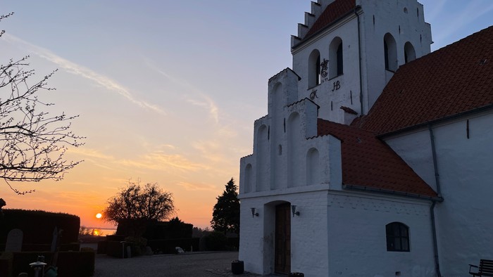 En fredfyldt kirke aftegnet mod en solnedgang med en rolig, åben gårdsplads.