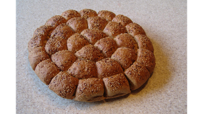 Ein rundes, mit Sesam bestreutes Brot auf einer weißen Oberfläche.
