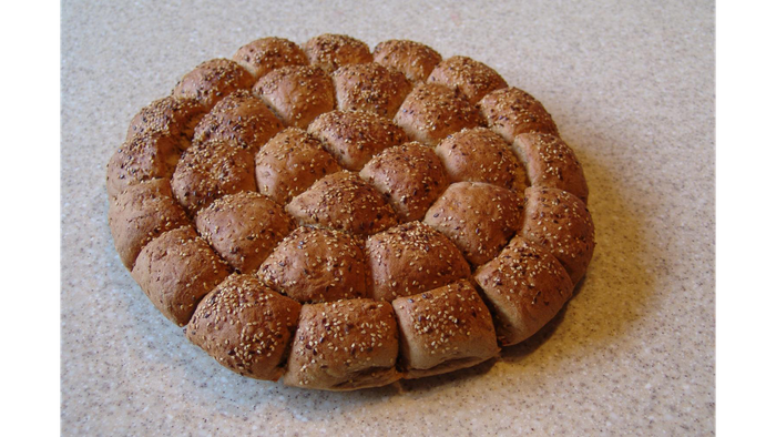 Ein rundes, mit Sesam bestreutes Brot auf einer weißen Oberfläche.