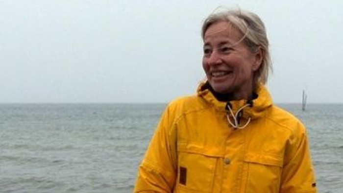 En kvinde i gult regnjakke står ved havet med en lighthouse i baggrunden