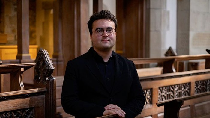 Mand står i kirke med briller og mørkt tøj.