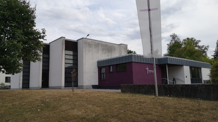 Moderne Gebäude mit Kreuzsymbol auf der Flaggenstange, umgeben von Bäumen und Gras.