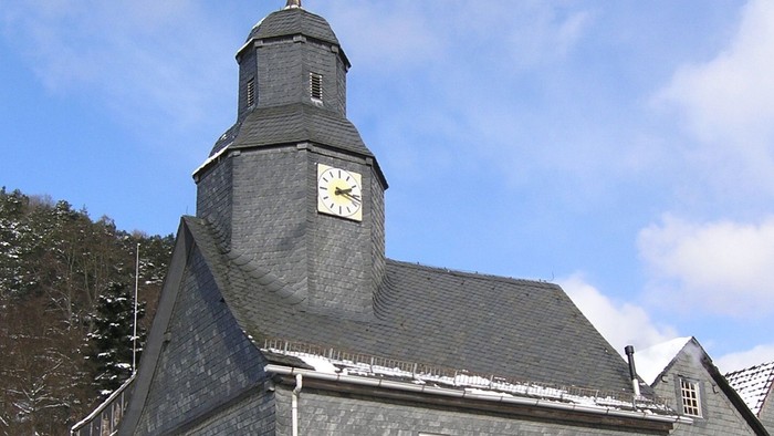 Graues Kirchgebäude mit Uhrturm und Schnee auf dem Dach