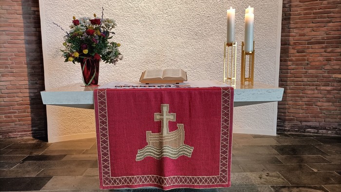 Altar mit rotem Tuch, Kerzen und Blumenarrangement