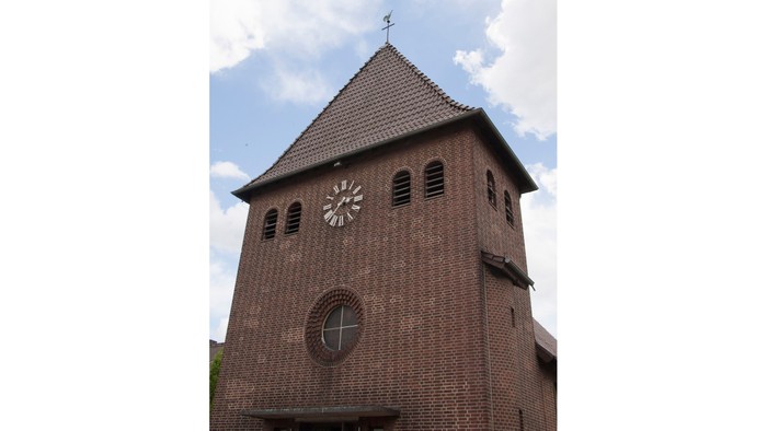 Der Kirchturm aus Ziegeln mit Uhr und Wetterfahne.