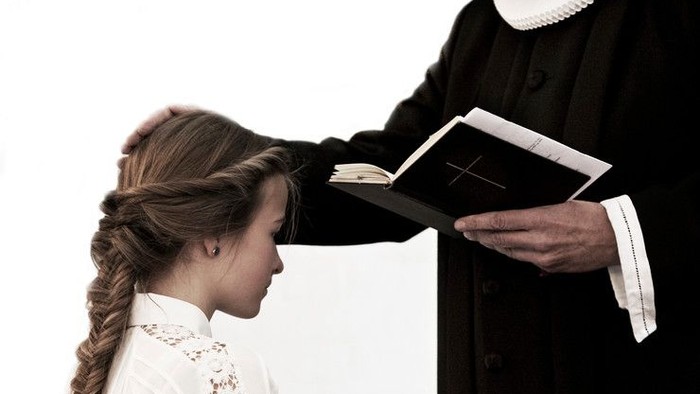 En præst viser en bog til en ung pige.