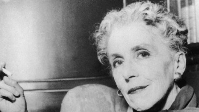 Ældre kvinde med krøllet hår, der holder en cigaret i en eftertænksom positur.