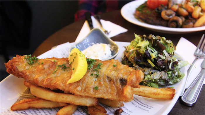 A plate of fish and chips with lemon wedge and salad