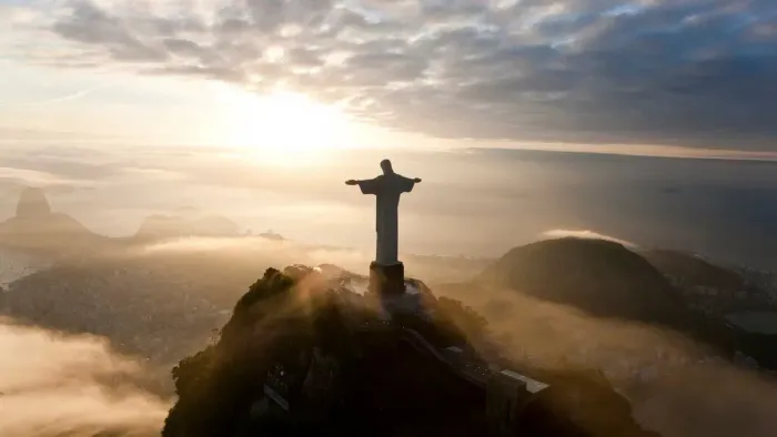Statue of Christ the Redeemer overlooking a city at sunrise.