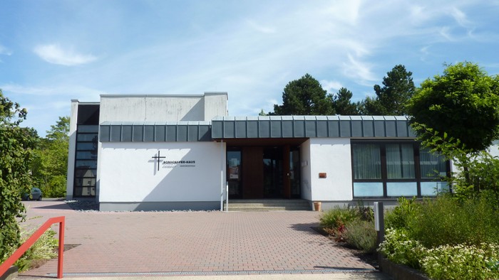 Moderne Kirchengebäude mit einem Kreuzsymbol an der Fassade, errichtet auf einer mit Backsteinen gepflasterten Plattform.