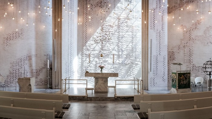 Moderne kirkeinteriør med minimalistisk design, indviklede mønstrede vægge, alter og træbænke.